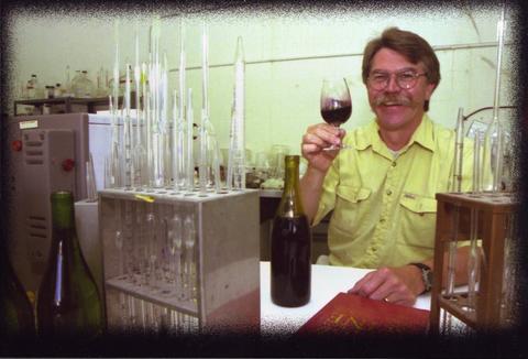 Photo of Barney Watson swirling a glass of wine surrounded by chemistry equipment.